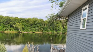 A house with a deck overlooking a lake, surrounded by rocks and plants. - River Retreat W/ HOT TUB/ Game room (Bristol)