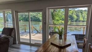 A room with a wooden table, a chair, and a view of a lake through large windows. - River Retreat W/ HOT TUB/ Game room (Bristol)
