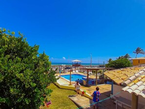 Zona de piscina con vista despejada al océano, un área de estar techada y un pequeño pabellón.