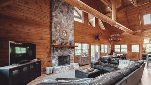A spacious living room with a stone fireplace, leather sofa, and a television on a wooden cabinet. - High Meadows Secluded Luxury Lodge, 20+ Acres, Hot Tub, Private Trails, Wifi (Rockbridge)