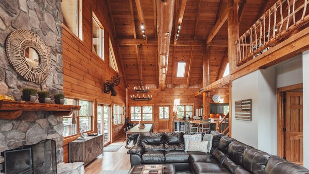 A spacious log cabin interior with a large leather sofa, stone fireplace, and a dining area. - High Meadows Secluded Luxury Lodge, 20+ Acres, Hot Tub, Private Trails, Wifi (Rockbridge)