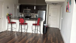 A modern kitchen with dark wood flooring, a dining area with red chairs, and a white door.
