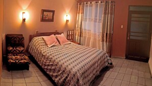 Un dormitorio con cama, dos luces en la pared, una silla, una puerta y una ventana con cortinas.