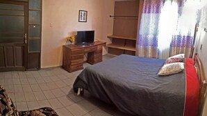 Un dormitorio con cama, escritorio con televisor, armario y ventana con cortinas.