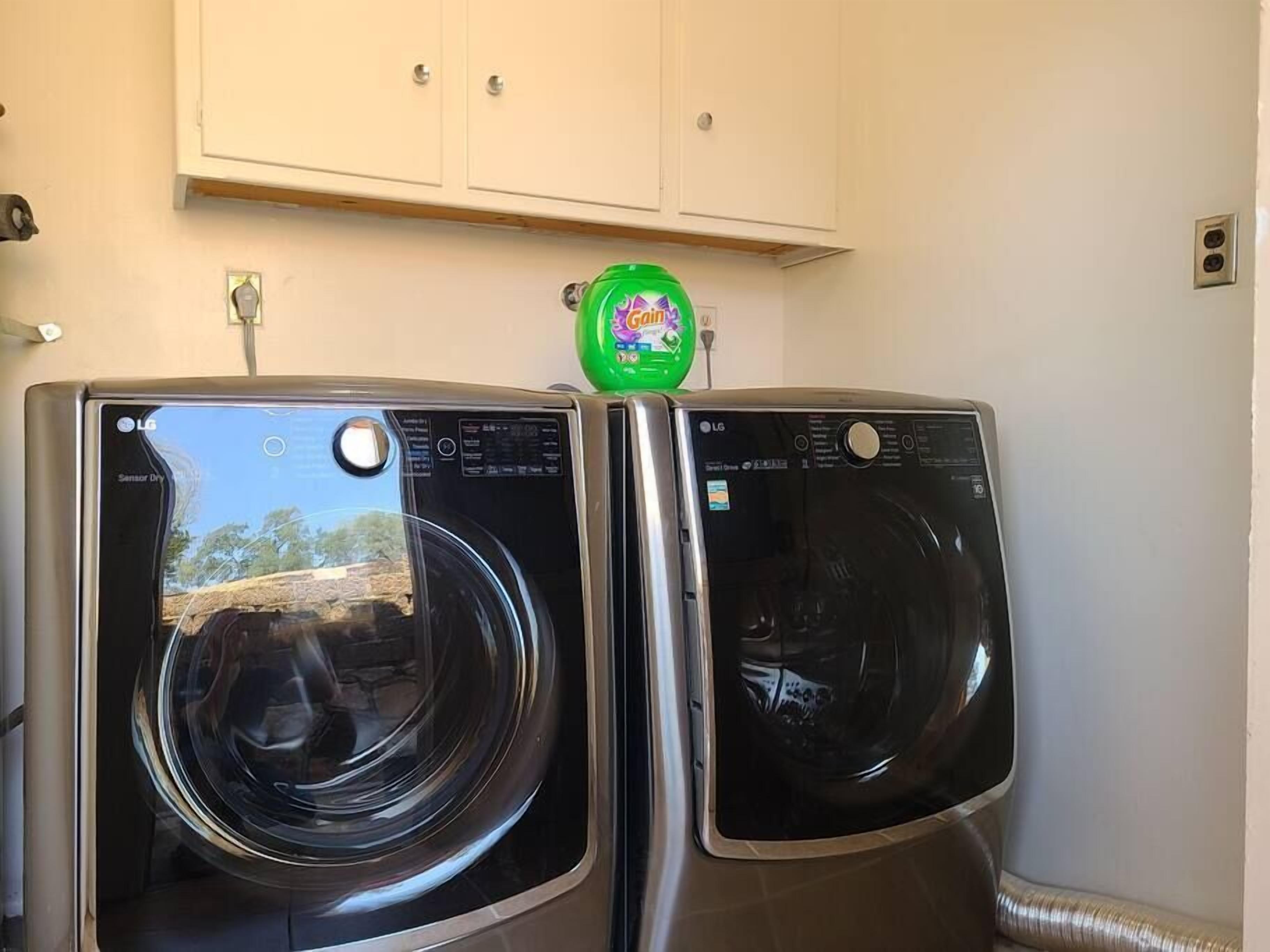 Two front-loading LG washing machines in a laundry room with a cabinet above.
