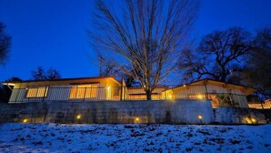 Un bâtiment moderne avec une façade en pierre, un grand arbre devant et un sol recouvert de neige.
