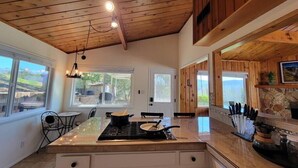 Une cuisine spacieuse dotée d’un îlot central, d’un plafond en bois, de grandes fenêtres et d’une cheminée en pierre.