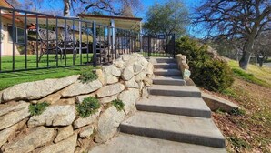 Un escalier en pierre mène à une entrée fermée par un portail, qui donne sur un patio abrité et aménagé avec du mobilier d’extérieur.