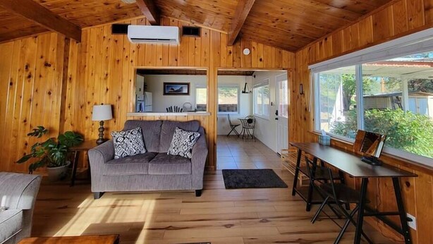 L'intérieur d'une cabane en bois, avec un canapé, une table à manger et un ventilateur de plafond.