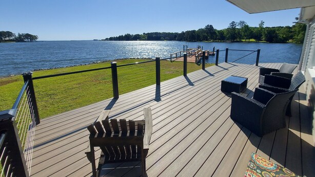 A wooden deck with outdoor furniture, a view of a lake, and a distant shoreline. - 10 Mile View on Lake Murray, SC, Putting Green, Hot Tub, Lake Edge Fire Pit (Gilbert)