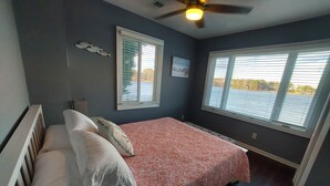 A bedroom with a bed, two windows, a ceiling fan, and a wall-mounted picture. - 10 Mile View on Lake Murray, SC, Putting Green, Hot Tub, Lake Edge Fire Pit (Gilbert)
