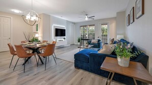 Ein modernes Wohnzimmer mit einem blauen Sofa, einem Esstisch mit Stühlen, einem Fernseher und einem Deckenventilator.