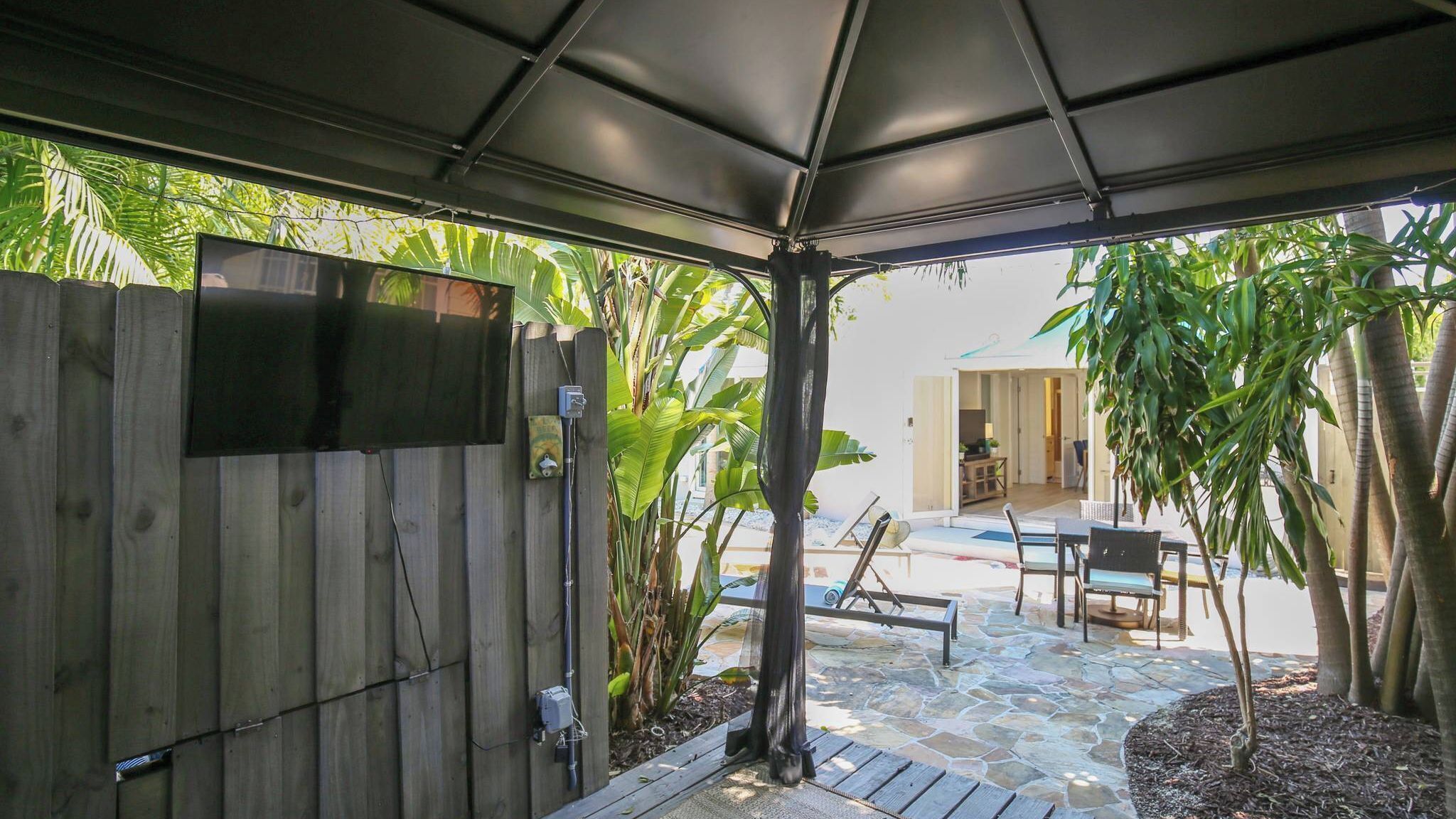 Une terrasse couverte, agrémentée d’une clôture en bois, de mobilier d’extérieur et de plantes tropicales.