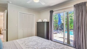 A bedroom with a bed, a dresser, a closet, and a view of an outdoor pool area. - Flagler's Oasis by Avantstay Tropical Key West Escape Private Pool Month Long Stays Only (Key West)