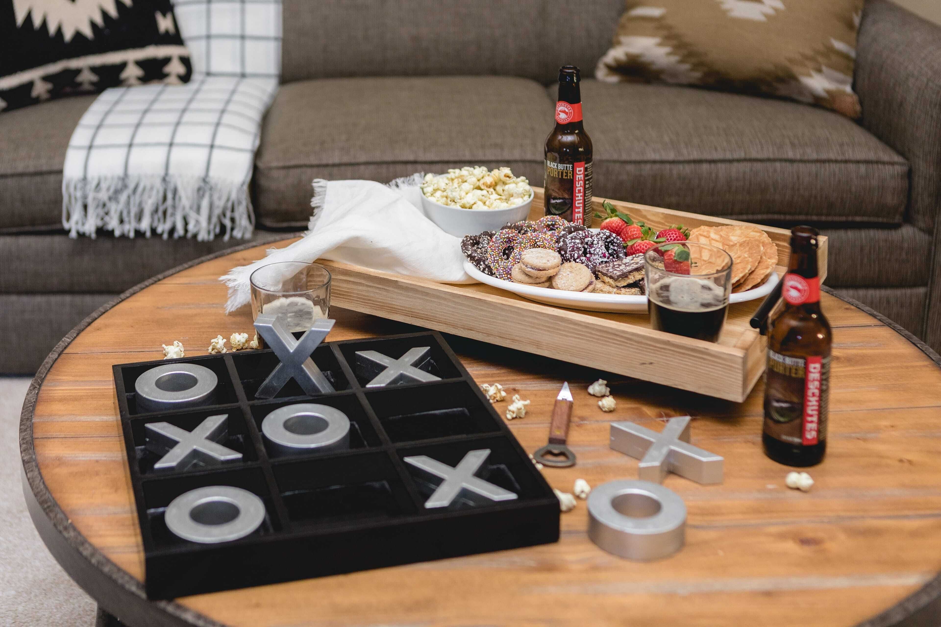 A cozy living room with a wooden coffee table, a board game, snacks, and a bottle of beer.