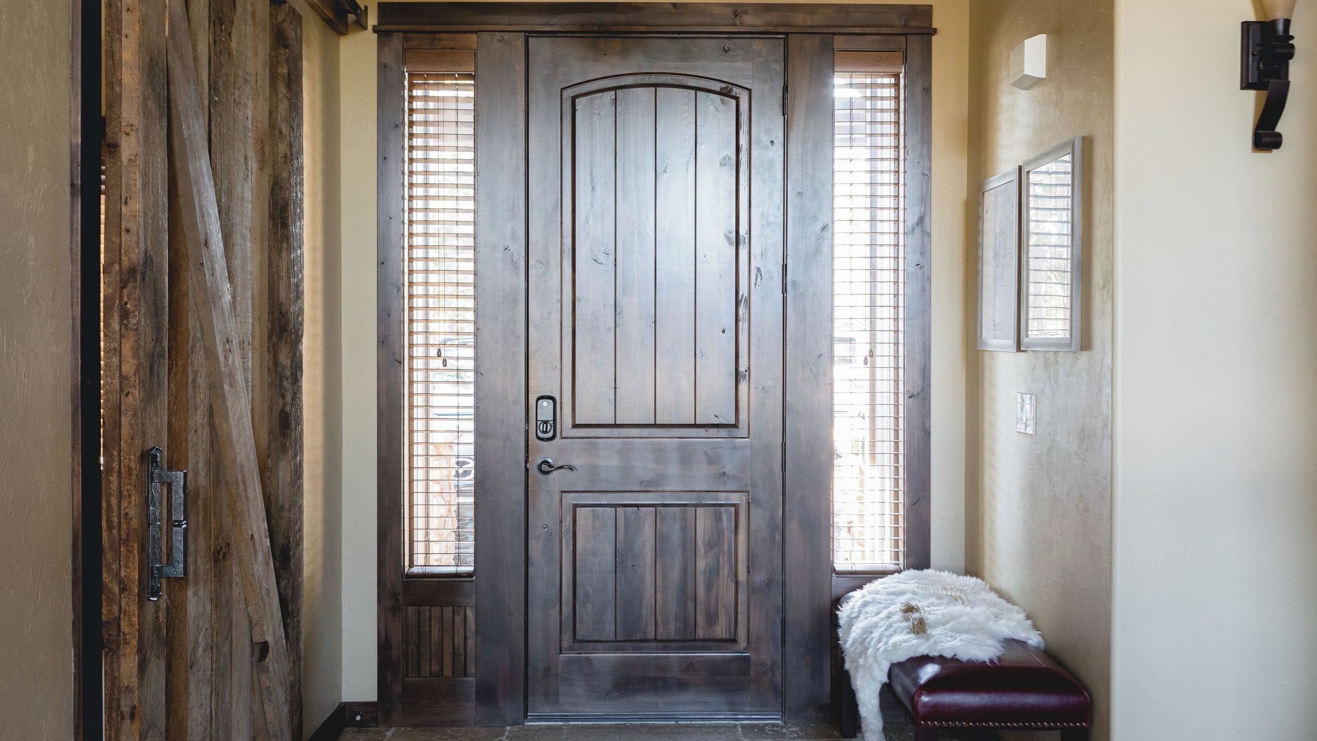 Una puerta de madera con un ventanal pequeño, un banco y una lámpara fijada a la pared.