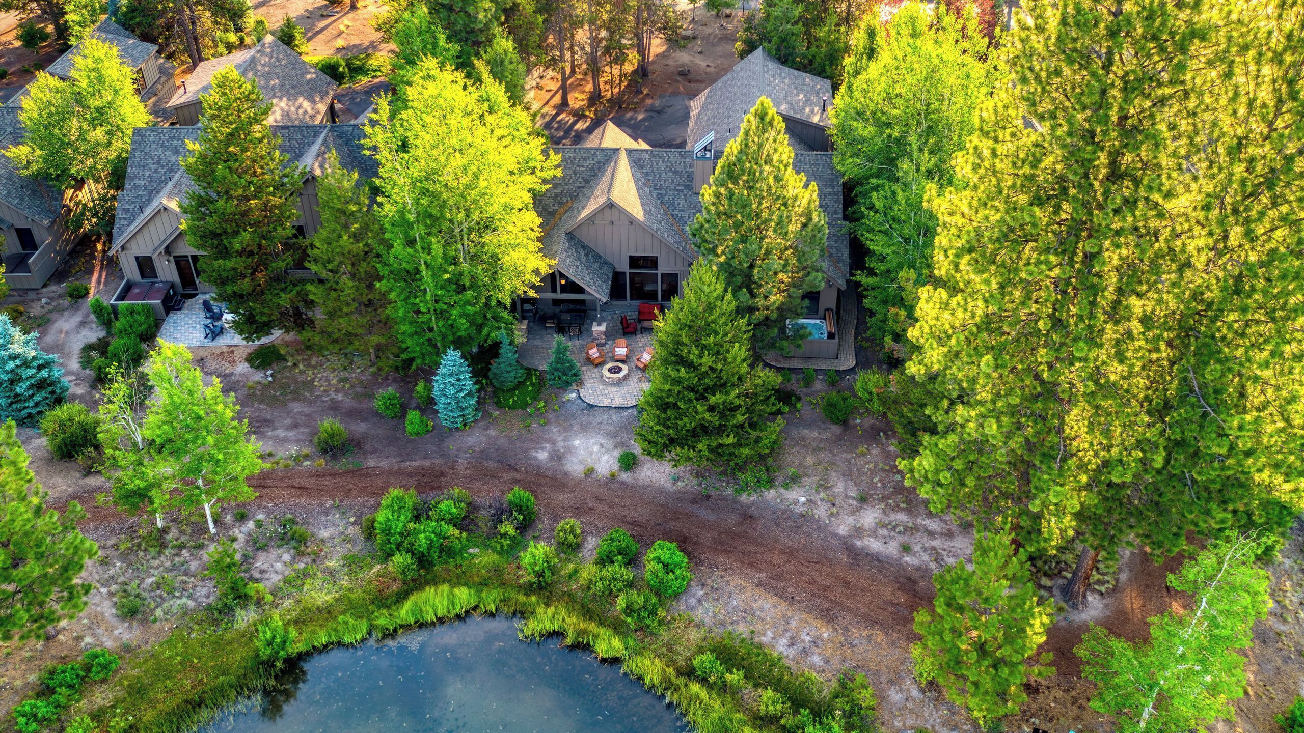 An aerial view of a residential area with multiple houses, a fire pit area, and a pond.