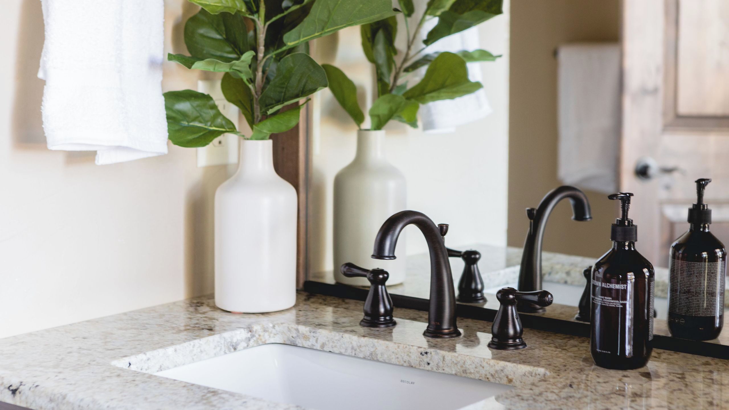 A bathroom with a white sink, black faucets, and two white vases with green plants.