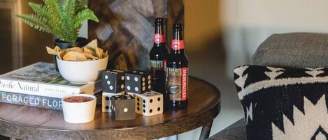 A table with a bowl of chips, two dice, a book titled 'Pacific Natural,' and two bottles of beer.