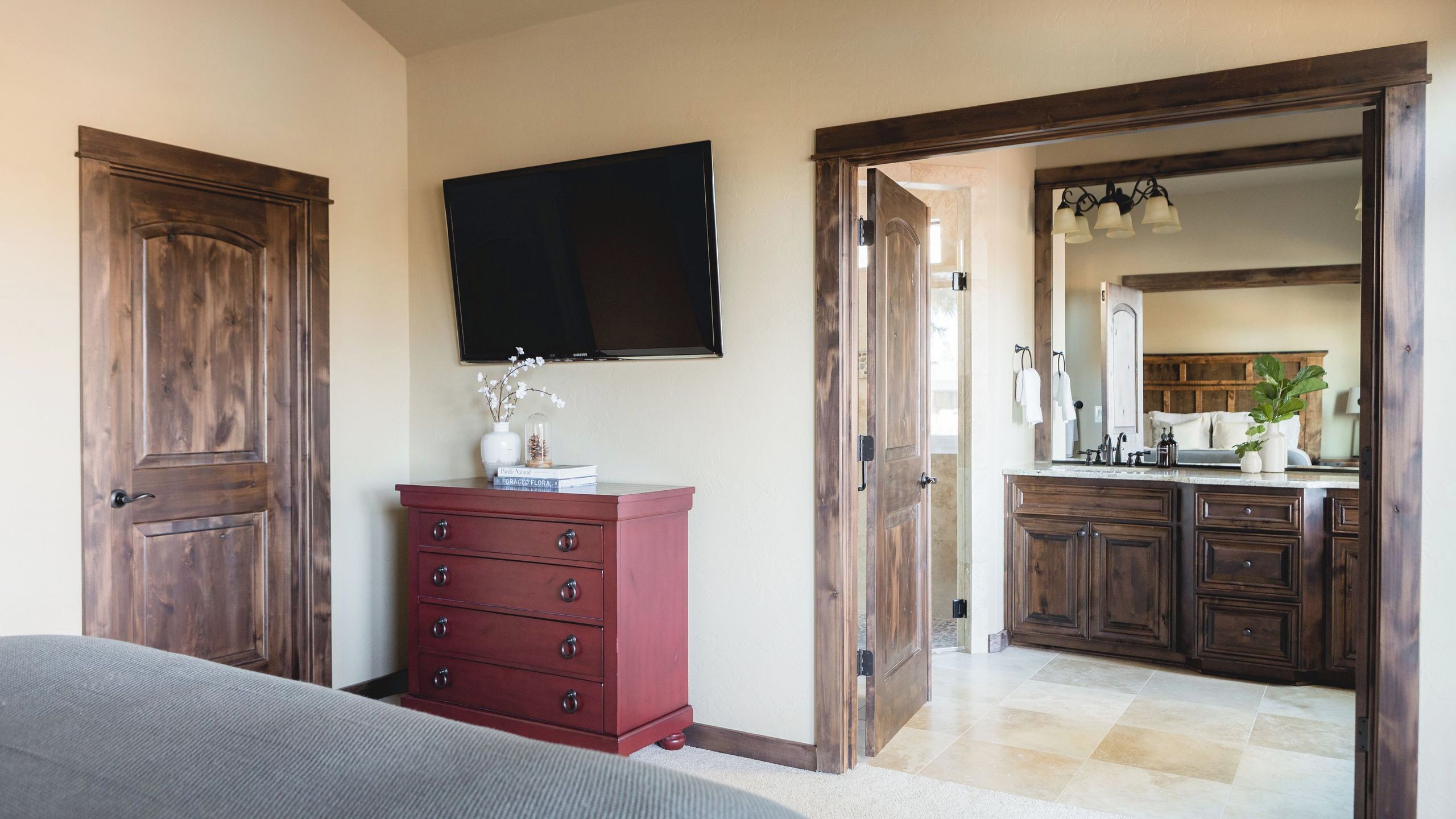 A bedroom with a bed, a dresser, a television, and a bathroom with a sink and mirror.