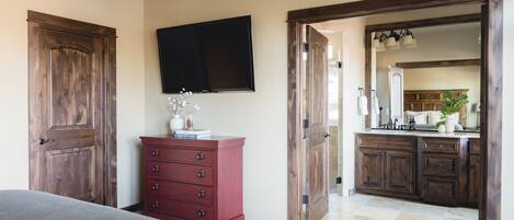 A bedroom with a bed, a dresser, a television, and a bathroom with a sink and mirror.
