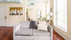 Ein Wohnzimmer mit grauem Sofa, einem Gemälde an der Wand und einem Fenster mit Jalousien.
