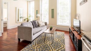 Ein Wohnzimmer mit grauem Sofa, Couchtisch, Fernseher und einem gemusterten Teppich.