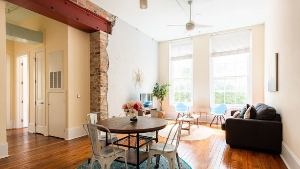 A spacious living room with hardwood floors, a round dining table with chairs, a black sofa, and a ceiling fan. - Bright & Sunny CBD FQ Convention Center Area Condo (New Orleans)