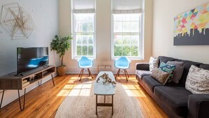 A modern living room with a TV, two blue chairs, a sofa, and a large window. - Bright & Sunny CBD FQ Convention Center Area Condo (New Orleans)