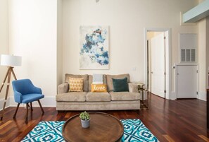 Una sala de estar con un sofá color beige, un sillón azul, una mesa de centro con una planta y un tapete estampado.