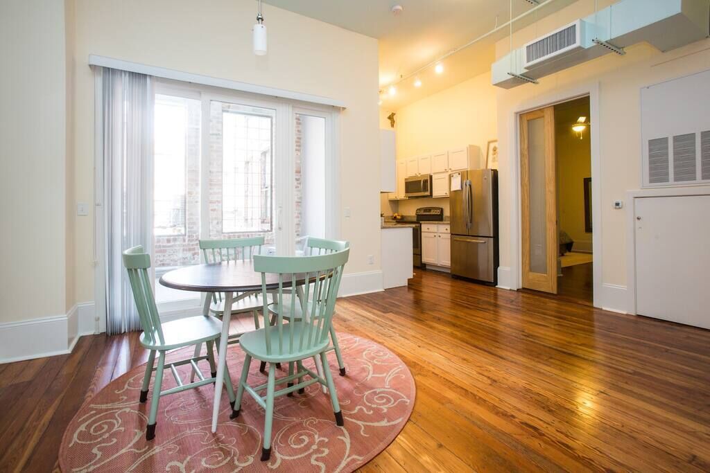 Una cocina moderna con electrodomésticos de acero inoxidable, un comedor con una mesa redonda y sillas, y piso de madera.