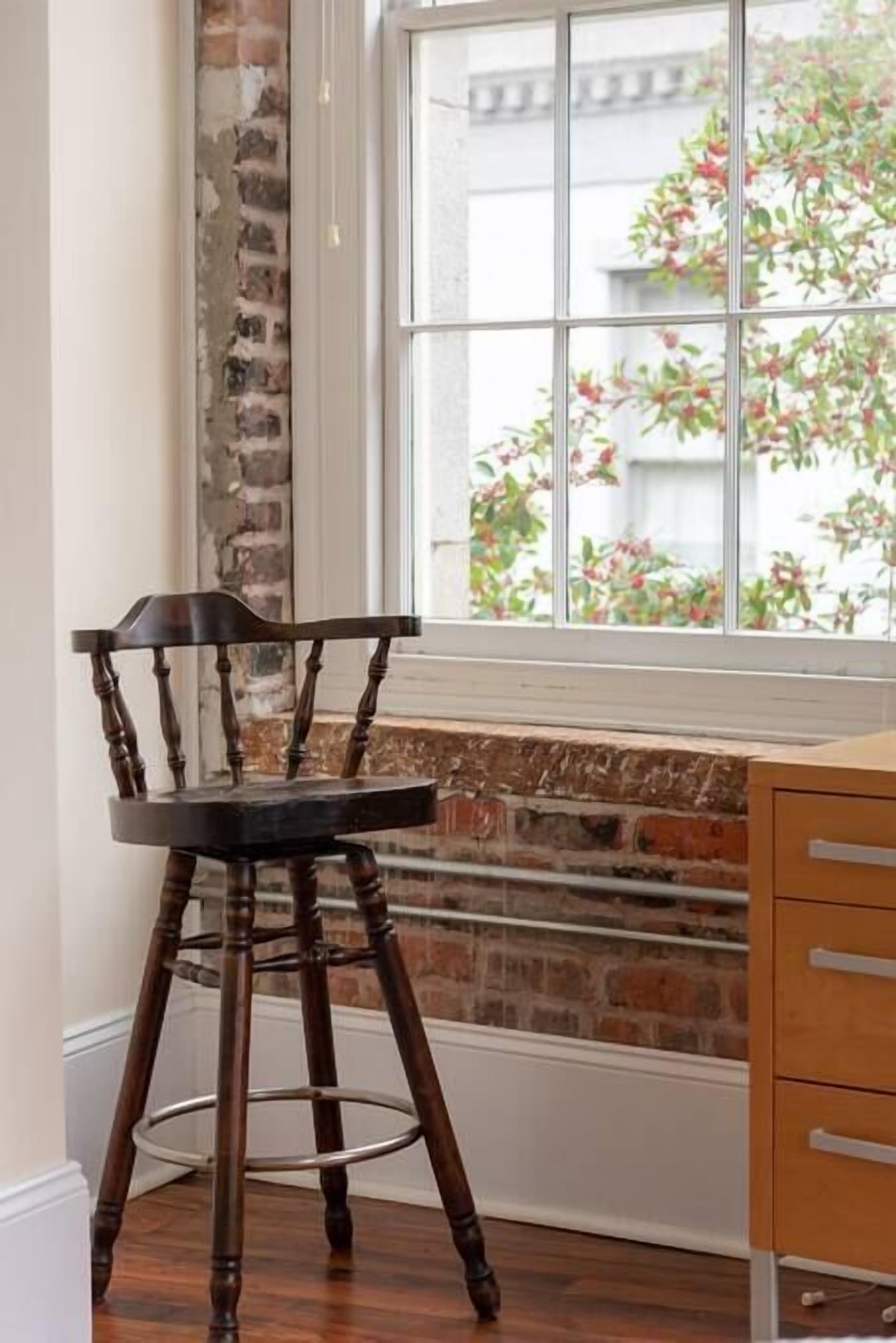 A corner room with a wooden chair, a window with a brick wall, and a wooden cabinet.