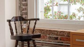 A corner room with a wooden chair, a window with a brick wall, and a wooden cabinet.