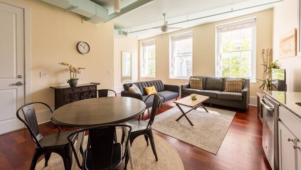 Uma sala de estar espaçosa com área de jantar, janelas amplas e cozinha moderna.