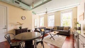 A spacious living room with a dining area, large windows, and a modern kitchen.