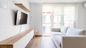 Ein modernes Wohnzimmer mit Flachbildfernseher, einem Holzkonsolentisch, einem weißen Sofa und einem Balkon mit Blick auf Gebäude.