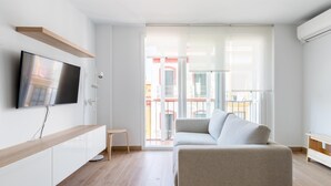 Ein modernes Wohnzimmer mit Flachbildfernseher, einer Couch und einem Balkon mit Blick auf Gebäude.