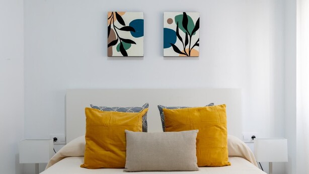 Een moderne slaapkamer met een groot bed, twee nachtkastjes en abstracte wanddecoratie.