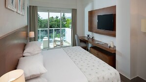 Habitación de hotel con cama, escritorio, televisor y balcón con vista a zonas verdes.