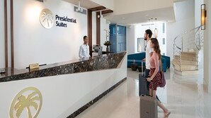 Una zona de recepción con mostrador de mármol, logotipo de una palmera y una escalera al fondo.