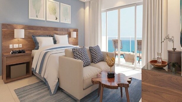 Habitación de hotel moderna con una cama grande, un sofá, una mesa de centro de madera y vista al océano.