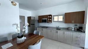 Une cuisine moderne avec des meubles de couleur bois clair, un réfrigérateur en acier inoxydable et un four encastré. On y trouve une table à manger avec des chaises et un vase rempli d’orchidées blanches.