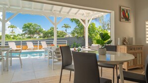A poolside area with a glass table, chairs, and a view of the pool and greenery. - Villa Green Caraibes, pool and view on the international golf of St-François (Saint Francois)