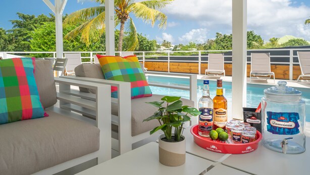 A poolside area with a covered seating area, a pool, and a bar area with drinks and snacks. - Villa Green Caraibes, pool and view on the international golf of St-François (Saint Francois)