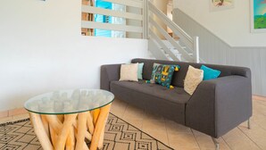 A living room with a grey sofa, a glass coffee table, and a staircase. - Villa Green Caraibes, pool and view on the international golf of St-François (Saint Francois)