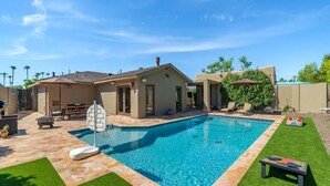 A residential backyard with a swimming pool, a patio area, and a small deck.