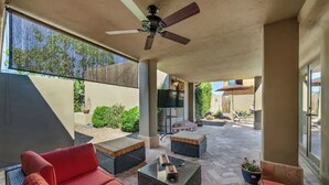 An outdoor patio area with red sofas, wicker tables, a ceiling fan, and a TV.