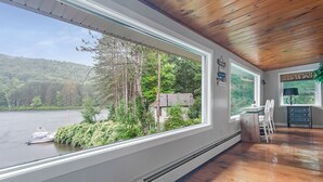 A room with a large window overlooking a lake, a wooden ceiling, and a small desk with a chair. - Lakefront, Kayaks, Firepit, great baseball stay! (Maryland)