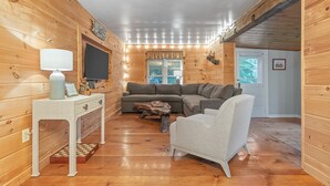 A cozy cabin interior with a wooden interior, a sofa, a chair, a small table, and a television. - Lakefront, Kayaks, Firepit, great baseball stay! (Maryland)
