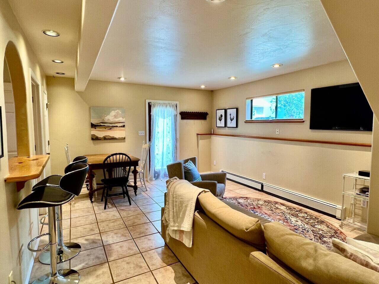 Un salon comprenant un canapé, des fauteuils, une table à manger et un téléviseur fixé au mur.